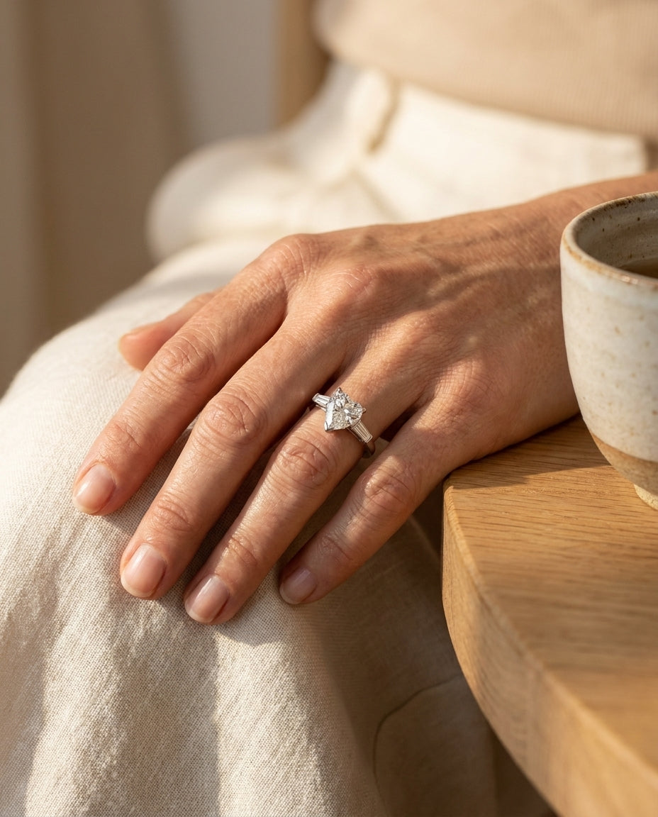 Platinum pear shaped diamond engagement ring worn on a hand resting on linen, editorial lifestyle photo