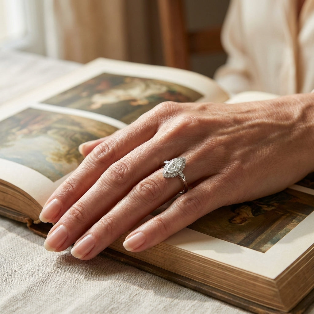 White gold marquise diamond engagement ring worn on a hand resting on an open book, editorial lifestyle photo