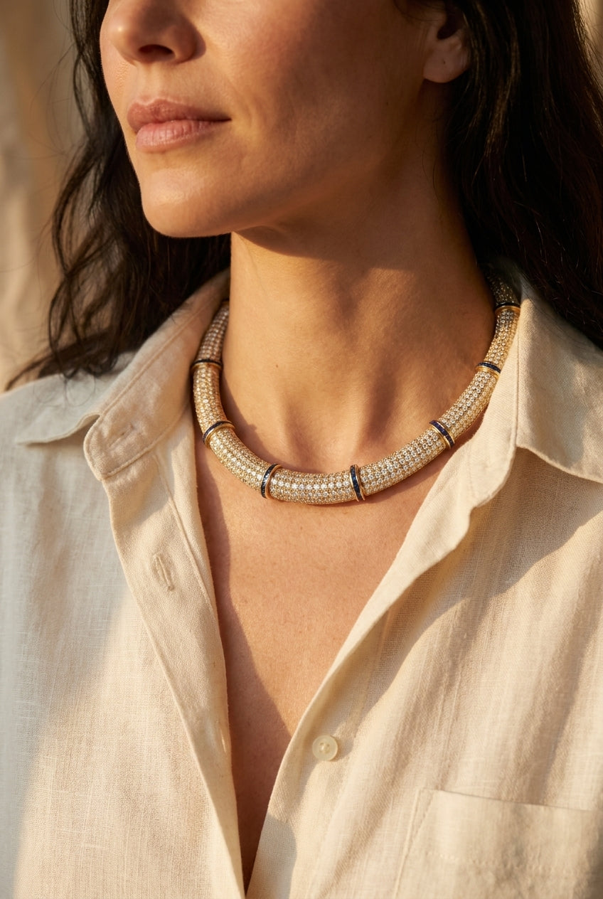 Yellow gold diamond and sapphire choker necklace worn at an open linen collar, editorial lifestyle photo